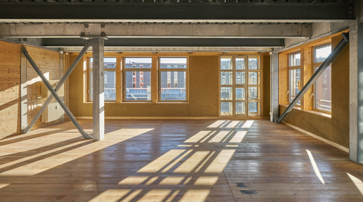 Interior of a converted industrial floor at K.118, with reclaimed timber flooring, exposed steel bracing, clay-plastered walls and salvaged windows in wooden frames.