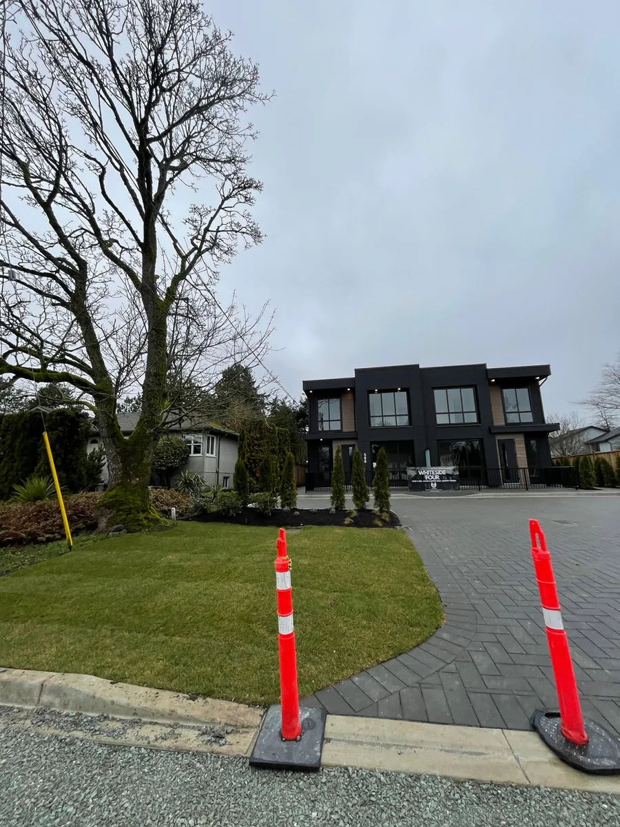 A newly built black four-plex on Whiteside Street with a paved forecourt and sales sign, standing beside a single-storey older house and a large bare tree.