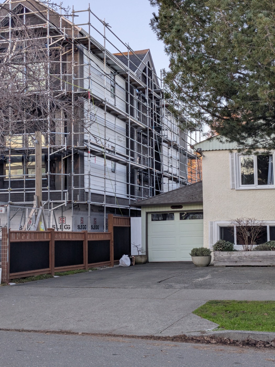 The Brooke Street construction site towering beside a neighbouring single-family house with a garage and mature trees