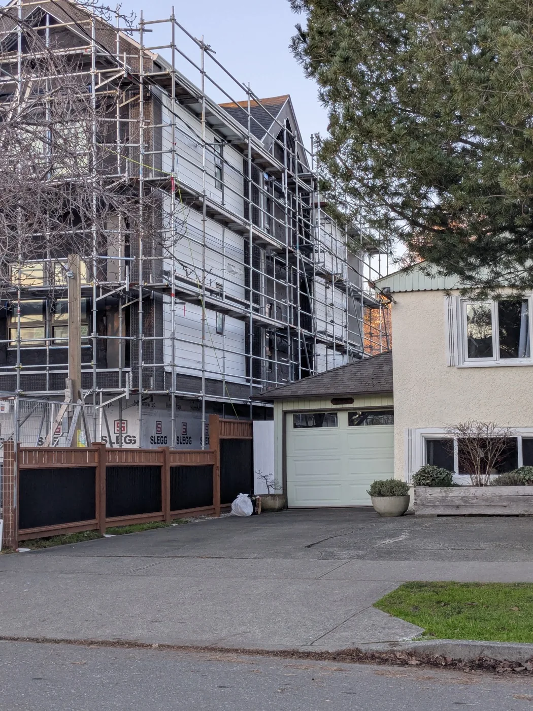 The Brooke Street construction site towering beside a neighbouring single-family house with a garage and mature trees